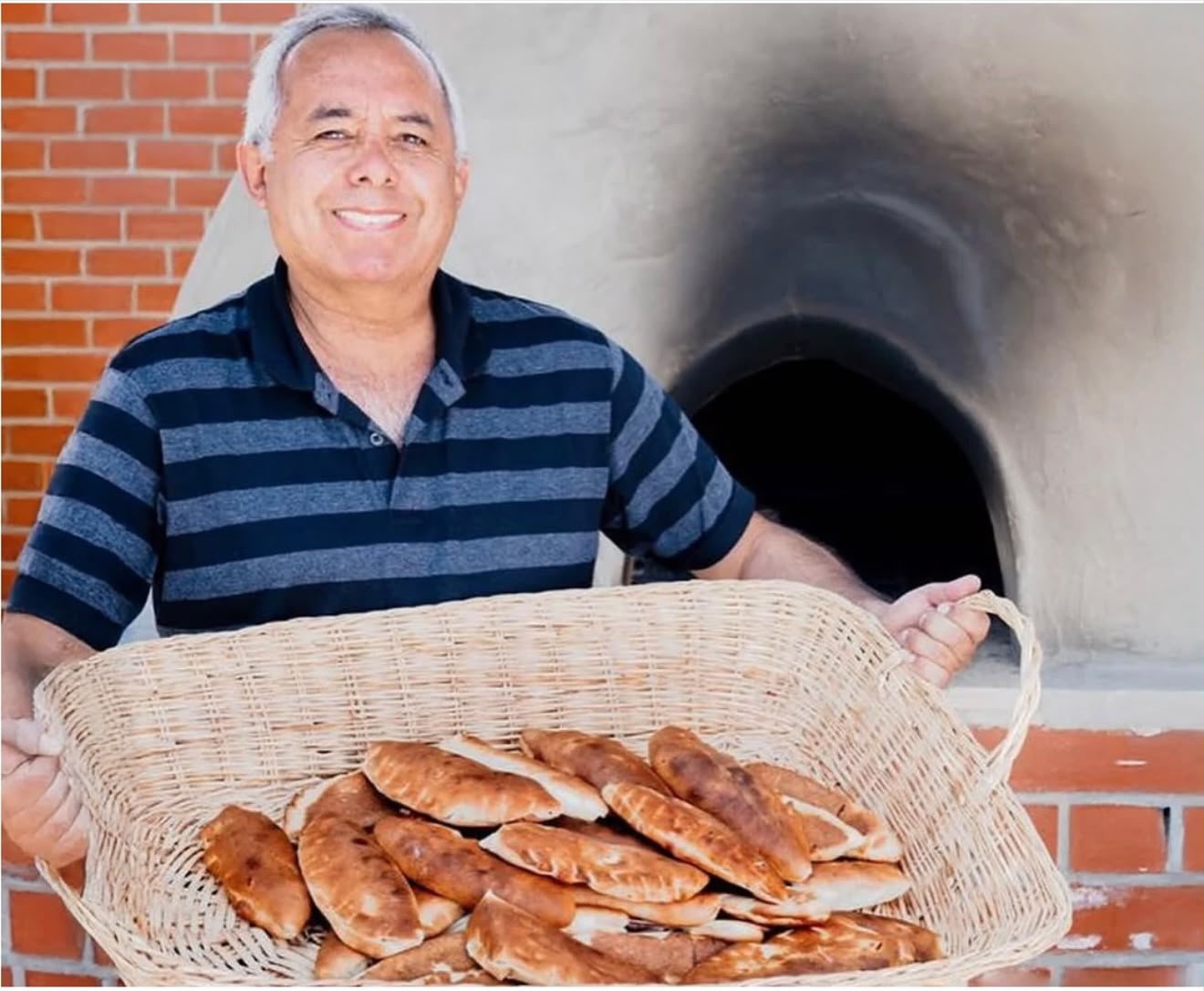 Señor sosteniendo una canasta de panes artesanales frente al horno